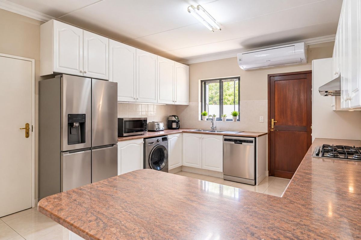A well-maintained kitchen featuring white cabinetry, granite countertops, a gas hob, integrated appliances, and an air conditioning unit.