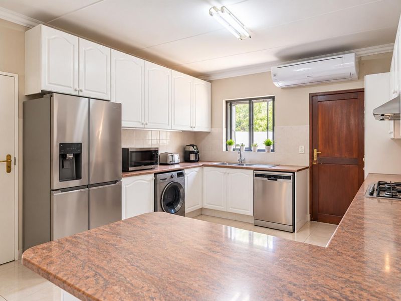 A well-maintained kitchen featuring white cabinetry, granite countertops, a gas hob, integrated appliances, and an air conditioning unit.