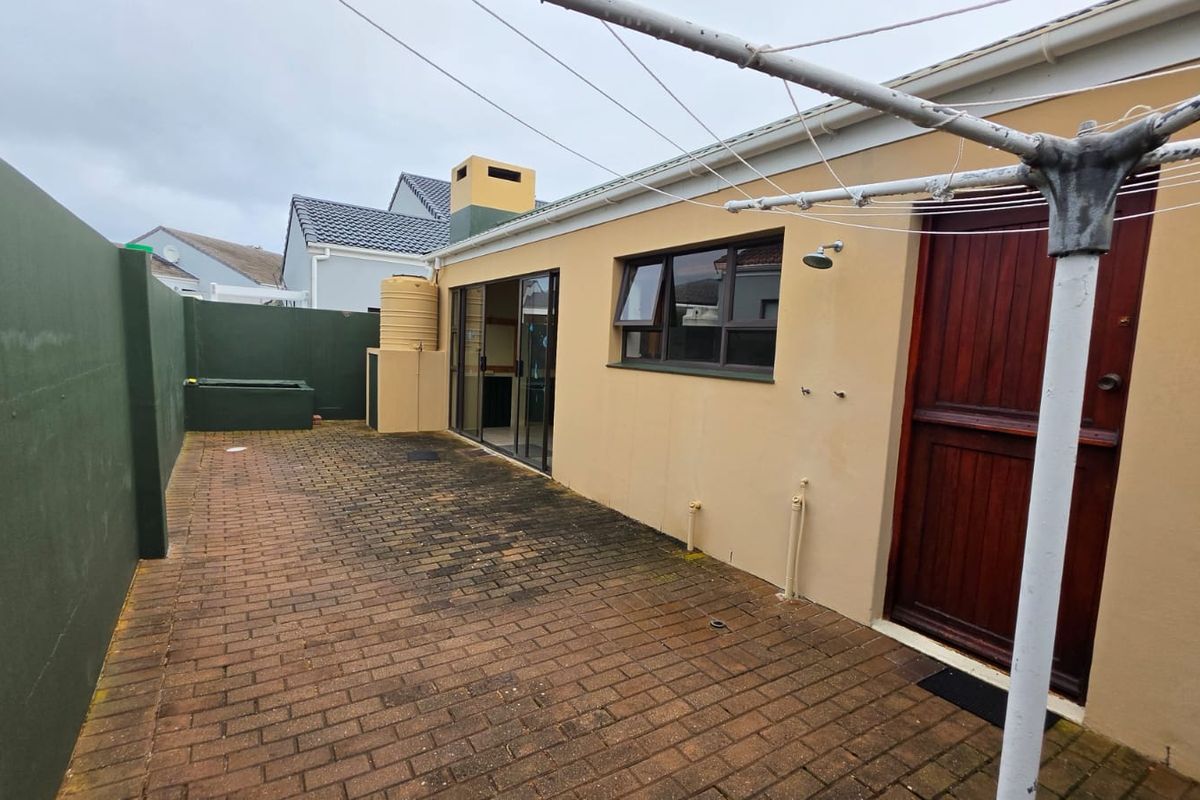 Rear exterior area featuring brick paving, an outdoor shower, a water tank, and access to the home via sliding glass doors.