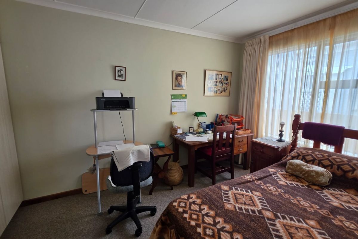 A functional bedroom featuring built-in cupboards, carpeted flooring, and large windows with curtain rails, offering a comfortable and practical living space.