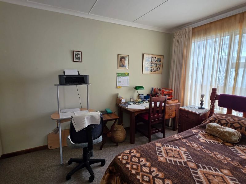A functional bedroom featuring built-in cupboards, carpeted flooring, and large windows with curtain rails, offering a comfortable and practical living space.