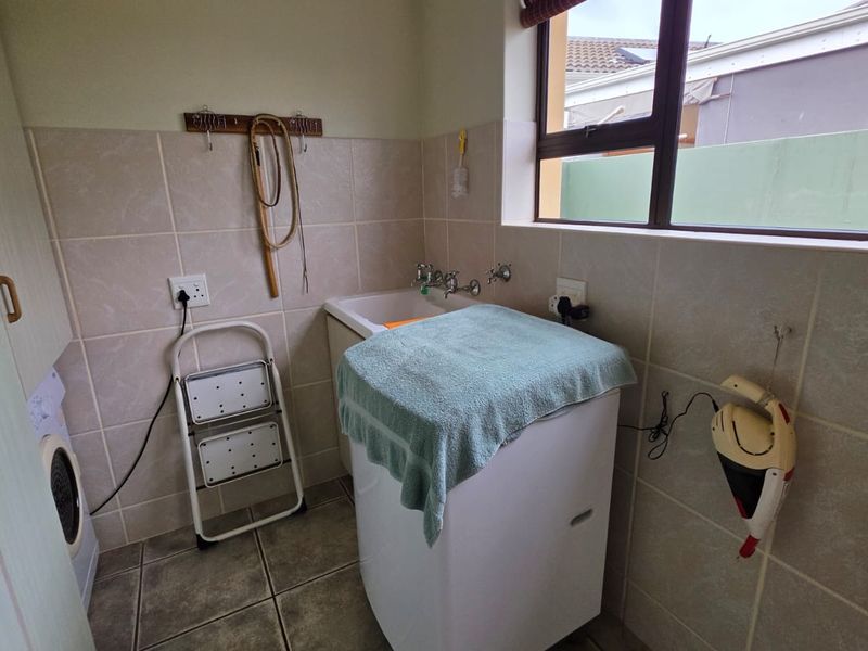 A functional laundry room featuring tiled walls, built-in cabinetry, and a dedicated laundry sink with plumbing fixtures.