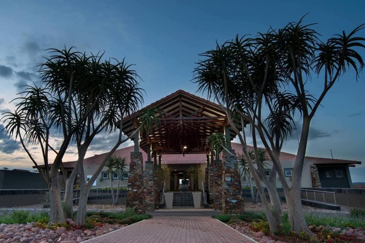 A striking front entrance featuring a timber-truss porte-cochere, stone-clad pillars, and a well-maintained paved walkway leading to the main building.