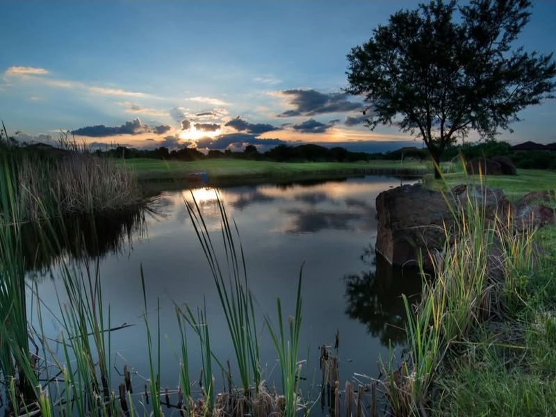 A scenic view of a tranquil pond and landscaped grounds at sunset, highlighting the natural beauty and peaceful atmosphere of the residential land.