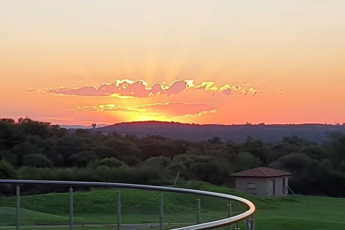 A scenic sunset view overlooking a landscaped residential area with a modern glass balustrade in the foreground.