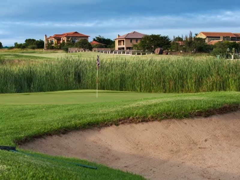A scenic view of a well-maintained golf course featuring a sand bunker and putting green with residential properties in the background.