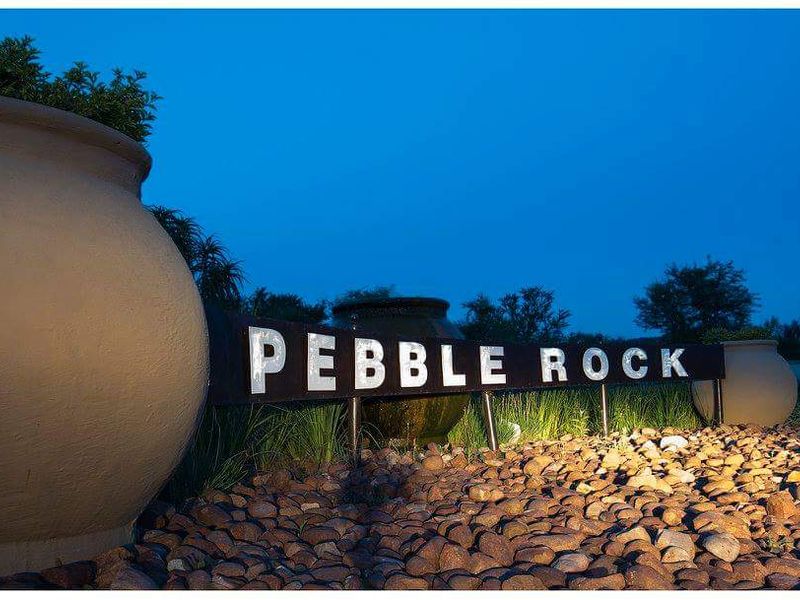 Illuminated entrance signage for Pebble Rock estate, featuring professional landscaping and decorative stone elements at dusk.
