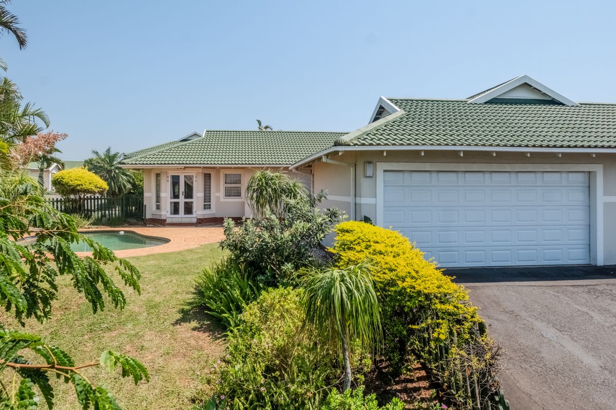Rear view of the townhouse featuring a tiled roof, double garage, swimming pool, and a well-maintained garden with a paved patio area.