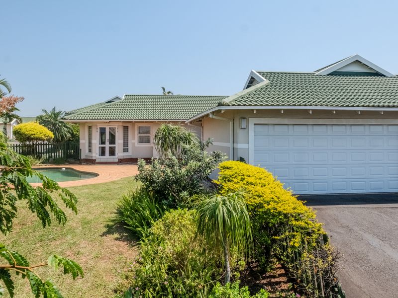 Rear view of the townhouse featuring a tiled roof, double garage, swimming pool, and a well-maintained garden with a paved patio area.
