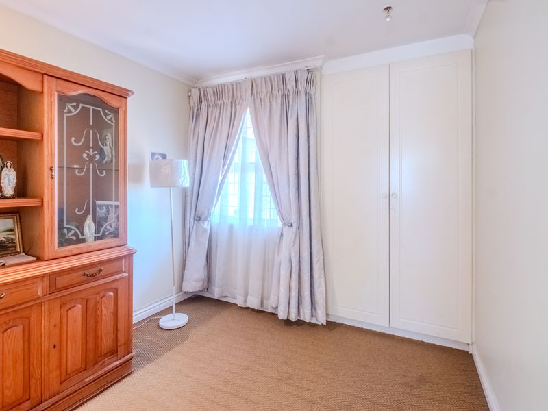 A bedroom featuring built-in wardrobe storage, carpeted flooring, and a window with curtains.