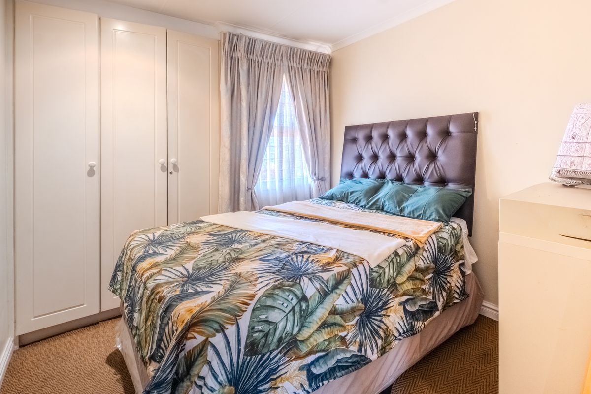 A well-maintained bedroom featuring built-in cupboards, carpeted flooring, and natural light through a window with curtain rails.