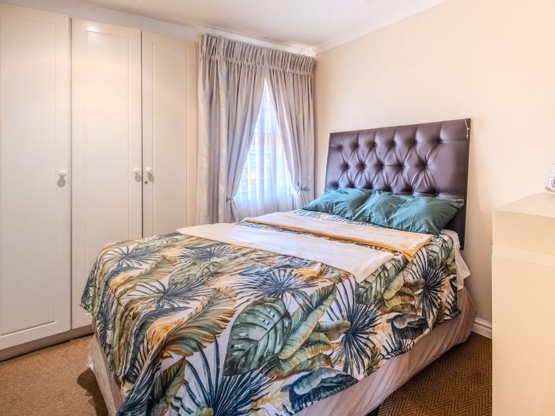 A well-maintained bedroom featuring built-in cupboards, carpeted flooring, and natural light through a window with curtain rails.