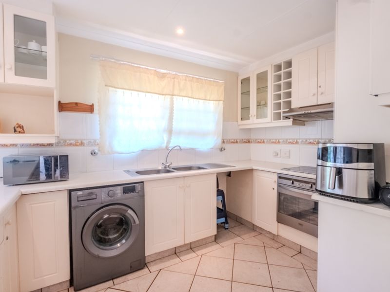A functional kitchen featuring white cabinetry, tiled backsplash, built-in oven with hob, extractor fan, and space for a washing machine.