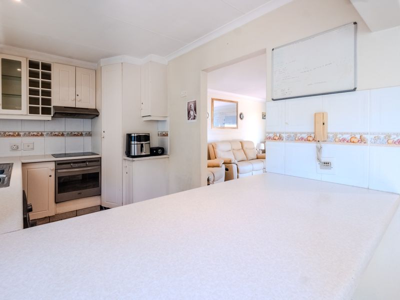 A functional kitchen featuring built-in cabinetry, an integrated oven and hob, and a breakfast counter, with an open-plan flow into the adjacent living area.