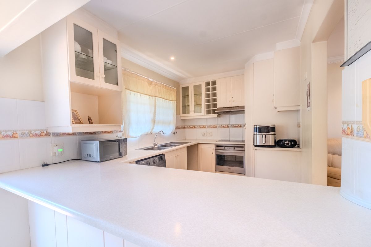A functional kitchen featuring built-in cabinetry, laminate countertops, a stainless steel sink, and integrated cooking appliances with a tiled backsplash.