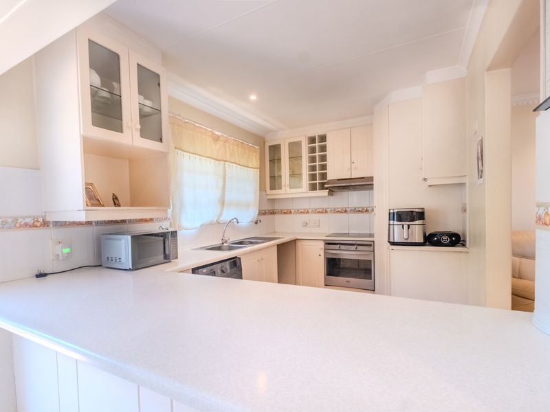 A functional kitchen featuring built-in cabinetry, laminate countertops, a stainless steel sink, and integrated cooking appliances with a tiled backsplash.