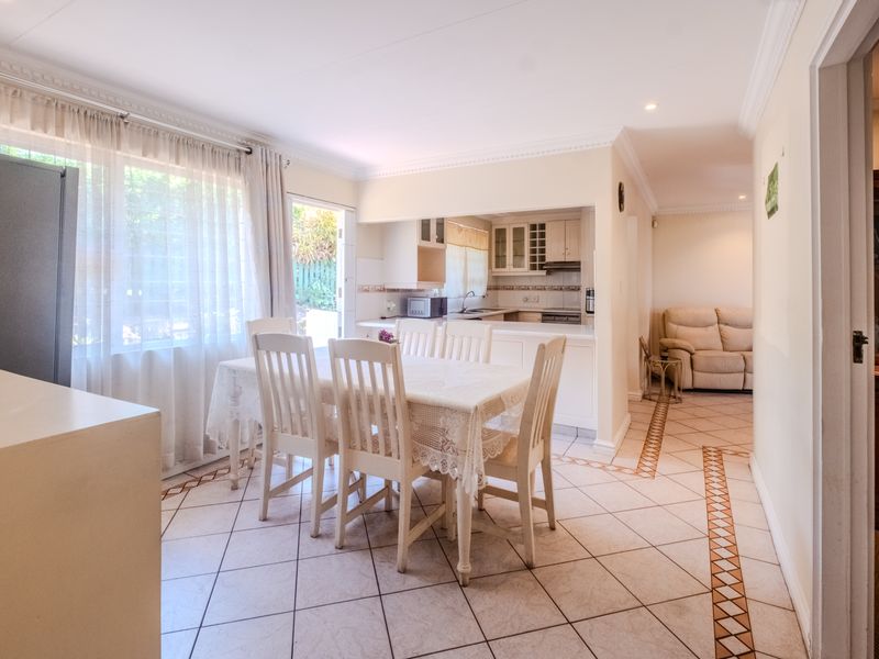 Open-plan dining area featuring tiled floors and coving, seamlessly connected to a functional kitchen with built-in cabinetry and appliances.