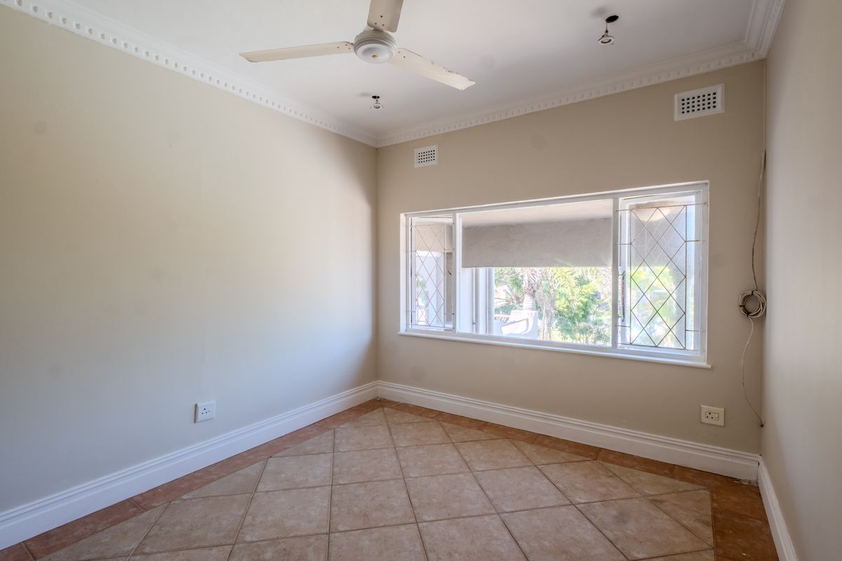 An empty bedroom featuring ceramic floor tiles, crown molding, a ceiling fan, and a large leaded glass window with natural light.