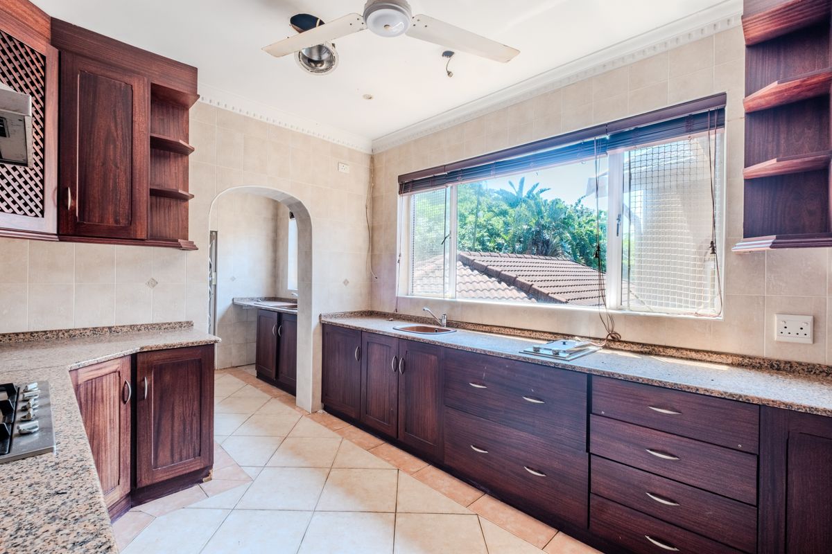 Spacious kitchen featuring dark wood cabinetry, granite countertops, tiled flooring, and an archway leading to a scullery area.
