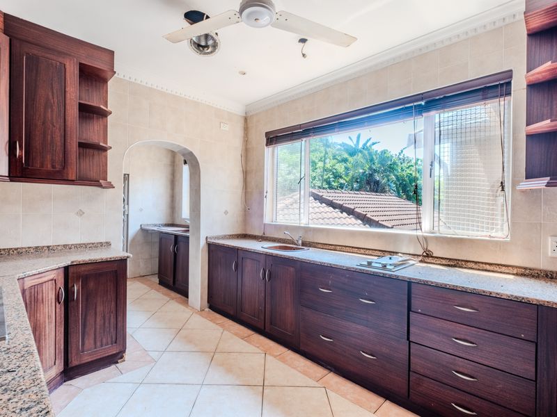 Spacious kitchen featuring dark wood cabinetry, granite countertops, tiled flooring, and an archway leading to a scullery area.