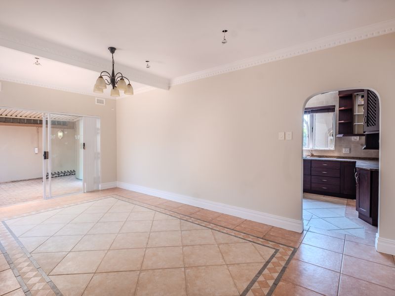 Spacious open-plan living area featuring tiled floors, crown molding, and an arched entryway leading to a functional kitchen, with sliding doors to the patio.