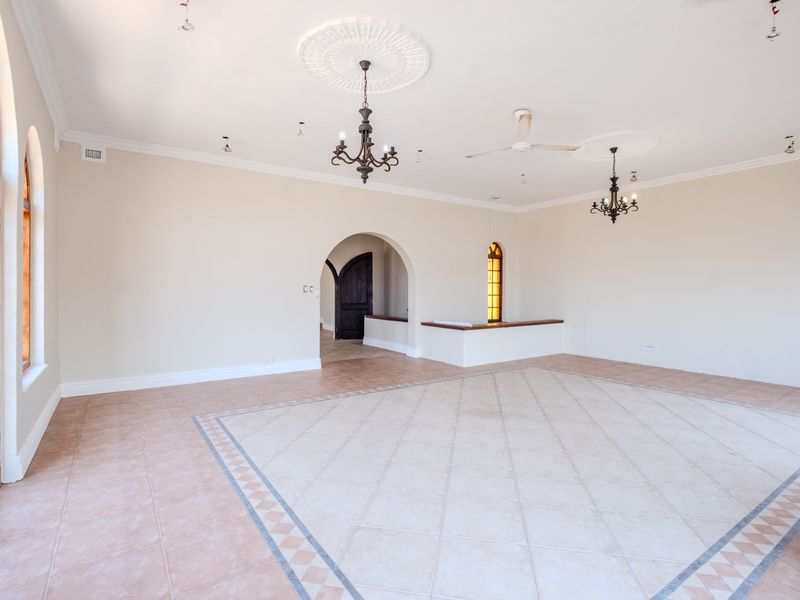 Spacious living area featuring decorative ceiling roses, chandeliers, arched windows, and tiled flooring with a distinct border pattern.