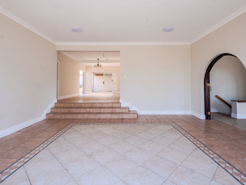 Spacious, empty living area featuring tiled flooring, a decorative archway leading to a staircase, and coved ceilings with recessed lighting.