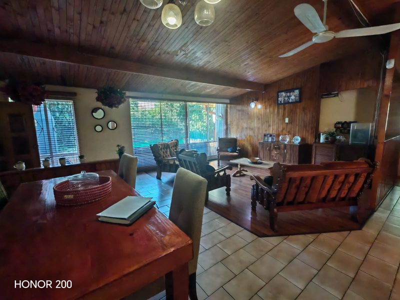 Spacious open-plan living and dining area featuring extensive timber wall and ceiling paneling, ceramic tiled flooring, and large windows with venetian blinds.