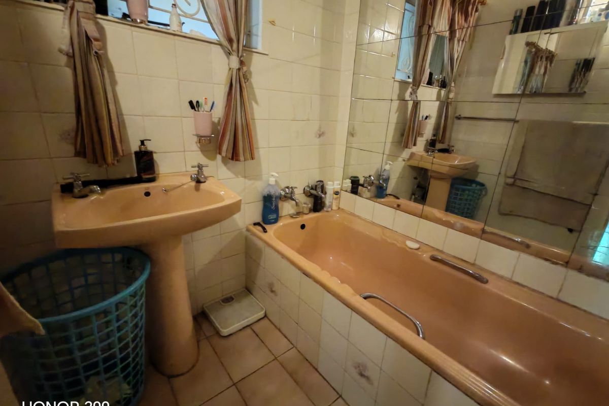 A dated bathroom featuring a peach-colored pedestal basin and bathtub, complemented by ceramic wall and floor tiles and a large wall-mounted mirror.