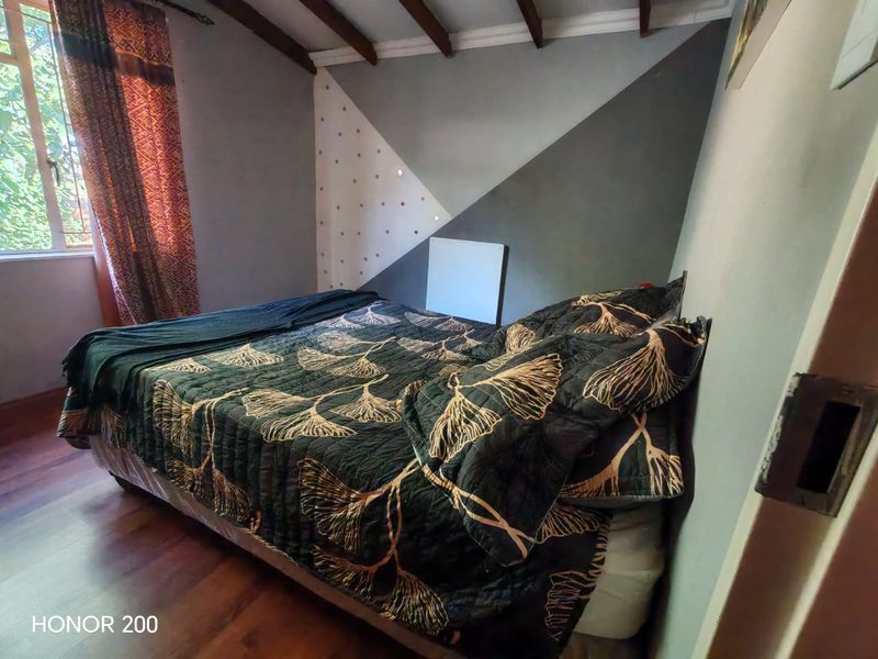 A bedroom featuring exposed timber ceiling beams, laminate flooring, and a window with natural light.