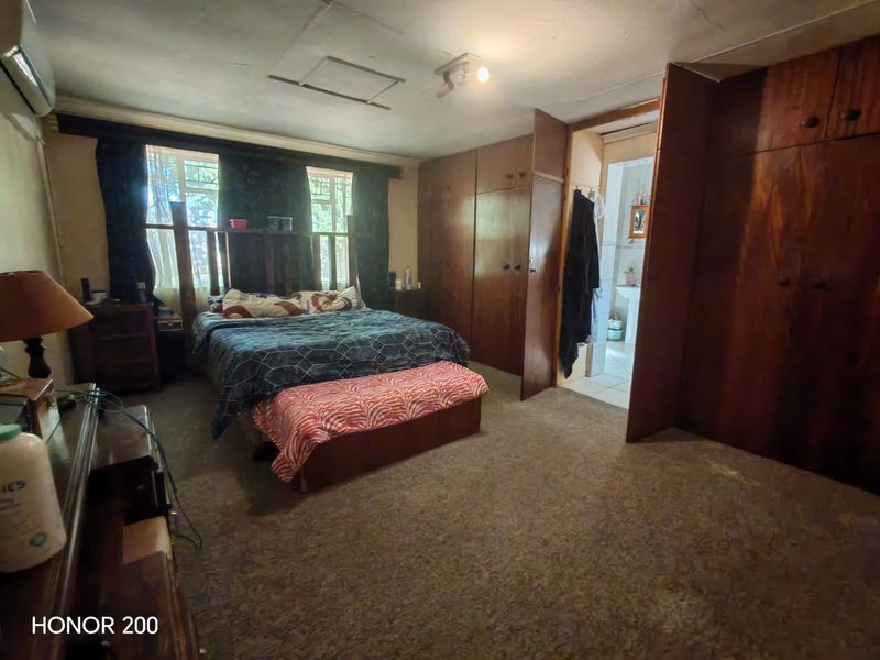 Spacious bedroom featuring extensive built-in wooden cabinetry, carpeted flooring, and an en-suite bathroom access point. The room requires cosmetic updates to modernize the finishes.