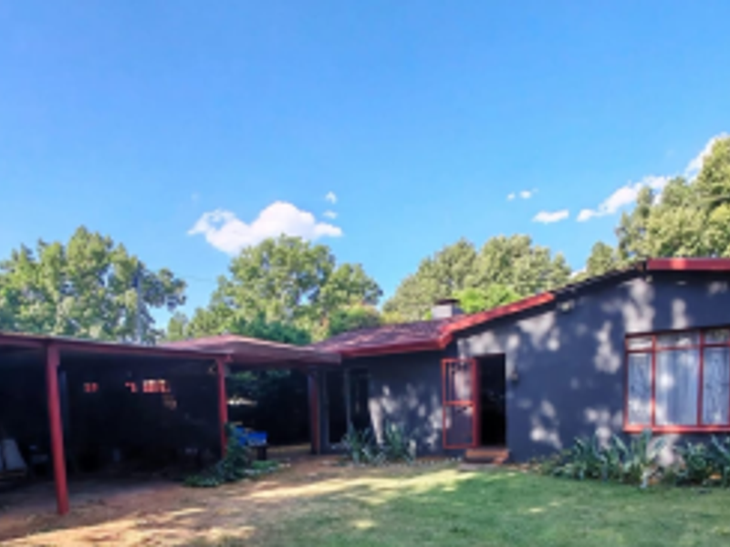 Rear view of the property featuring a dark-painted exterior, a spacious carport, and a large garden area.