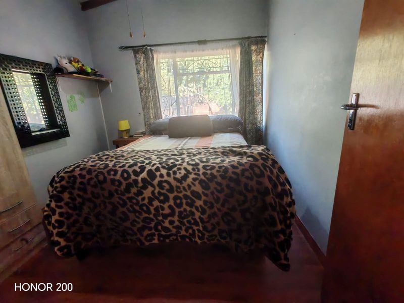 A compact bedroom featuring laminate flooring, a window with a security gate, and a wooden door.
