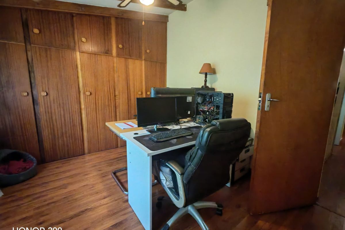 A bedroom featuring built-in wooden cupboards, exposed timber ceiling beams, and laminate flooring, currently utilized as a home office space.