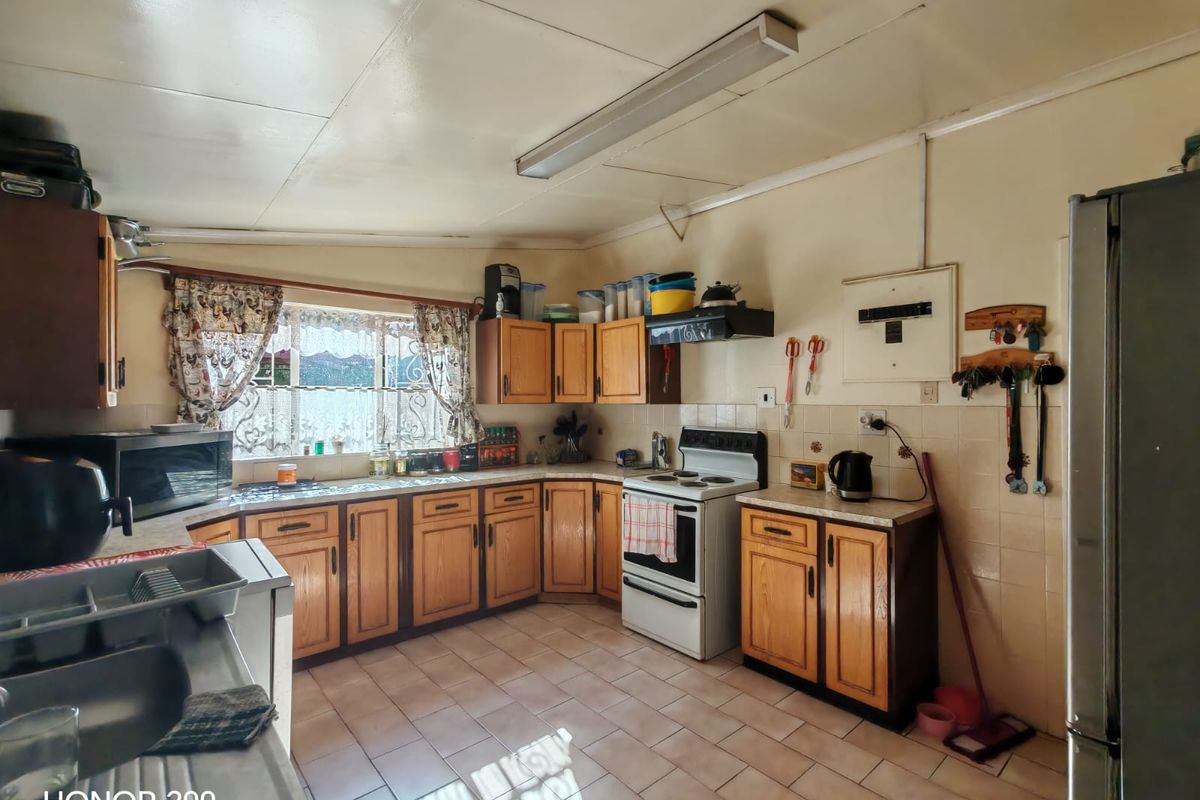 A functional kitchen featuring wooden cabinetry, tiled flooring, and a tiled backsplash, offering a dated aesthetic with potential for modern renovation.