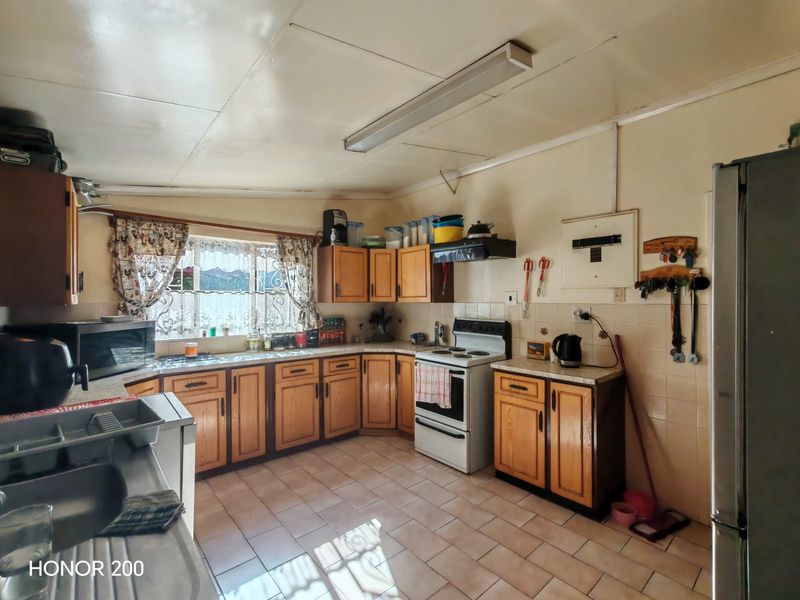 A functional kitchen featuring wooden cabinetry, tiled flooring, and a tiled backsplash, offering a dated aesthetic with potential for modern renovation.