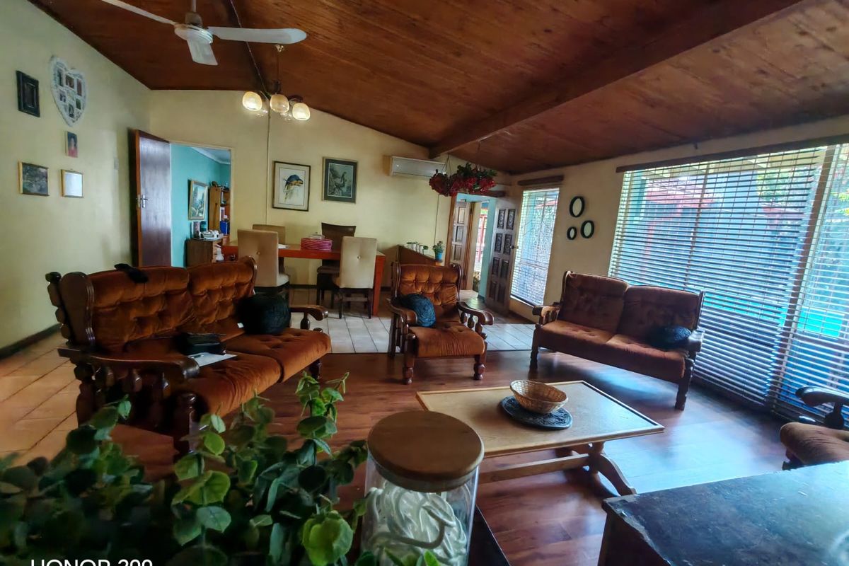Spacious living room featuring a vaulted timber ceiling, ceiling fan, timber flooring, and large windows with venetian blinds.