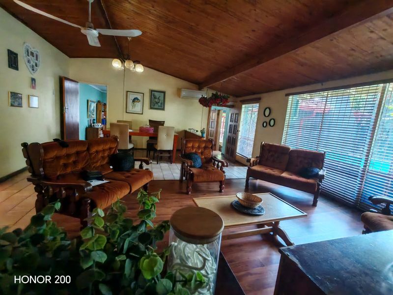 Spacious living room featuring a vaulted timber ceiling, ceiling fan, timber flooring, and large windows with venetian blinds.