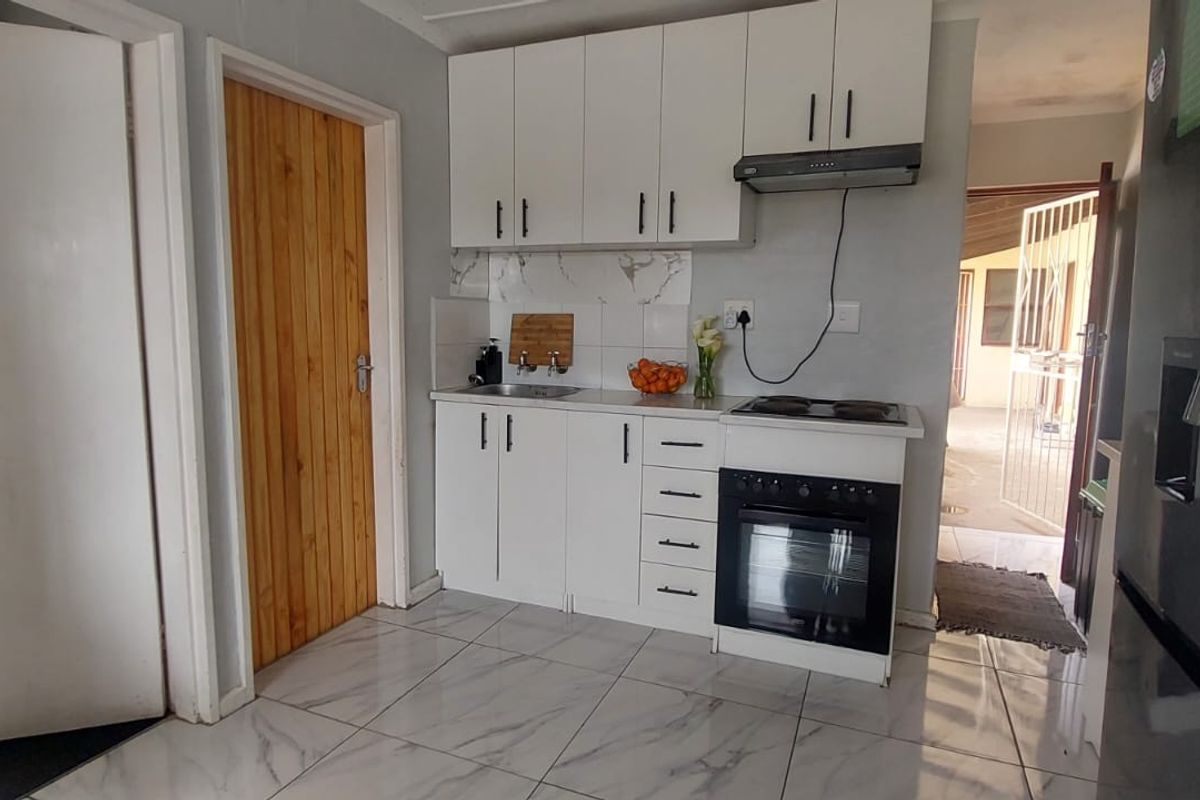 A compact kitchen featuring white cabinetry, a built-in oven with hob, extractor fan, and marble-look tiled flooring.