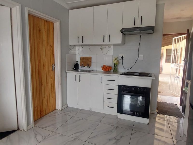 A compact kitchen featuring white cabinetry, a built-in oven with hob, extractor fan, and marble-look tiled flooring.