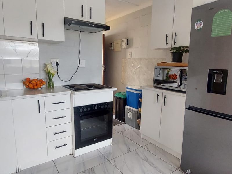 Compact kitchen featuring white cabinetry, tiled backsplash, built-in oven with hob, and extractor fan, finished with modern floor tiles.