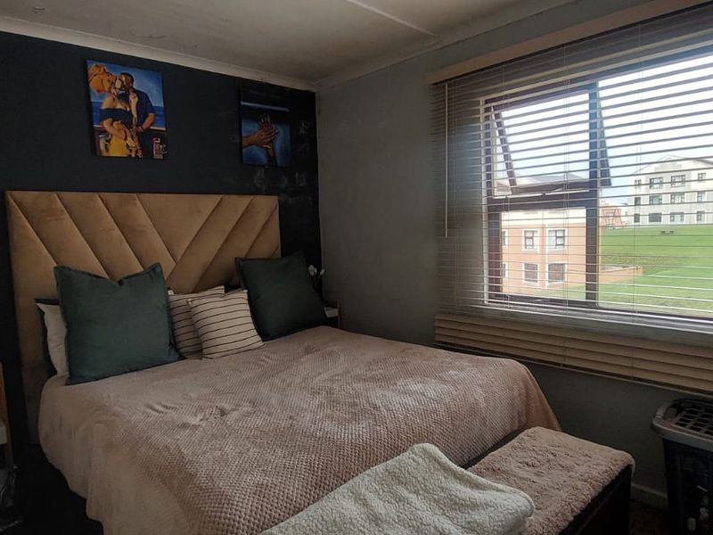 A cozy bedroom featuring an accent wall, venetian blinds, and natural light, offering a comfortable space for rest.