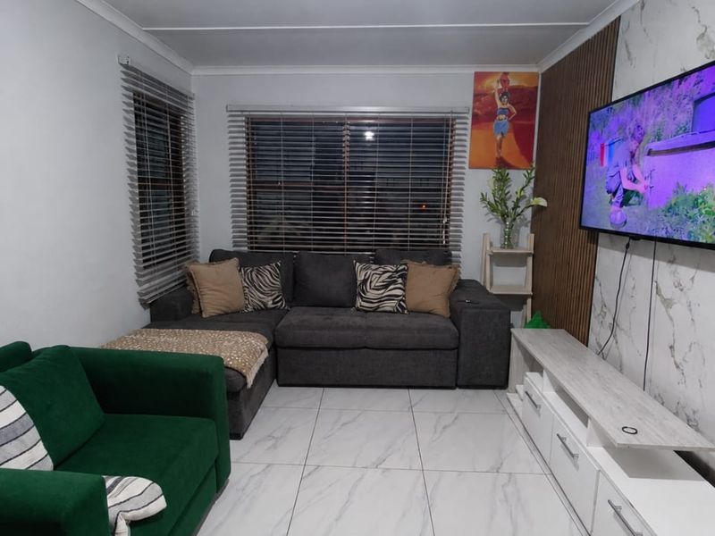 A well-maintained living room featuring modern marble-look floor tiles, a decorative slatted wood feature wall, and venetian blinds.