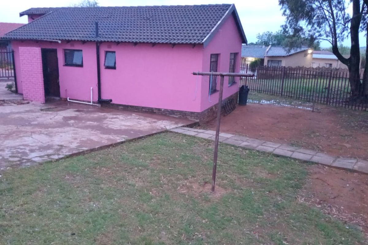 Rear view of the property featuring a concrete patio area, a small garden space, and metal perimeter fencing.