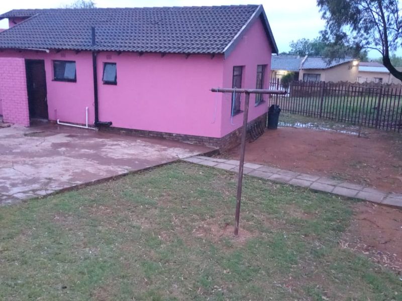 Rear view of the property featuring a concrete patio area, a small garden space, and metal perimeter fencing.