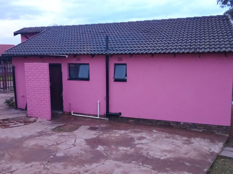 Rear view of a detached residential structure featuring a tiled roof, pink painted brick walls, and an adjacent cracked concrete driveway area.