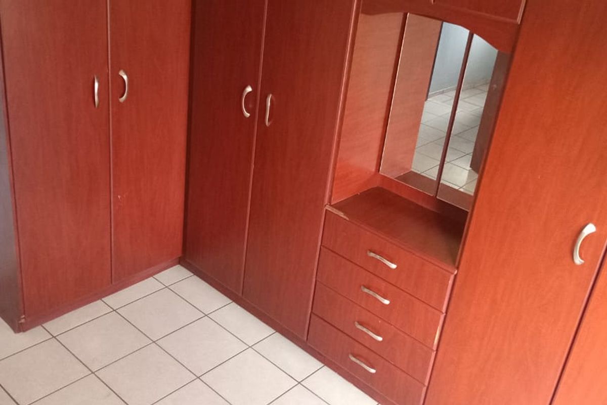 A bedroom featuring extensive built-in wooden cabinetry with integrated drawers and tiled flooring throughout.
