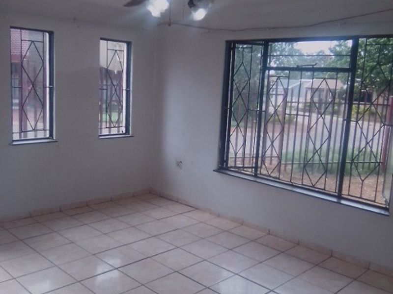 An empty living room featuring tiled flooring, a ceiling fan, and windows fitted with security bars.