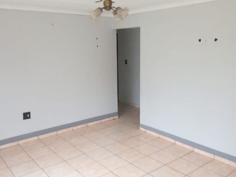 An empty living room featuring neutral wall paint, ceramic floor tiles, and a central ceiling light fixture, ready for personalization.