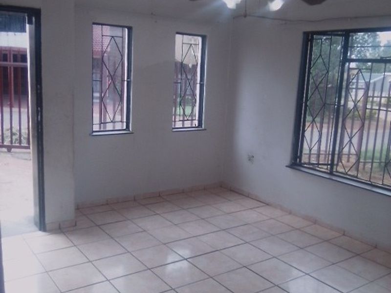 An empty living room featuring tiled flooring, a ceiling fan, and security bars on the windows, providing a blank canvas for interior design.